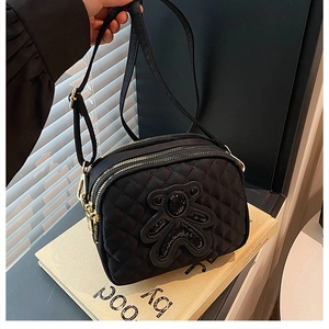 Close-up of quilted black crossbody bag with sequin bear and triple zip pockets