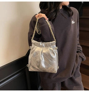 Detail of silver quilted handbag featuring metallic finish and gold chain strap on model