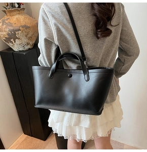 Close-up of minimalist black leather bucket bag with top handle and adjustable shoulder strap