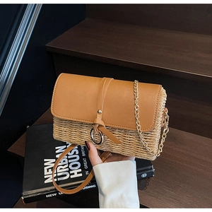 Detail view of straw woven crossbody bag with PU leather flap on wooden stairs