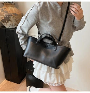 Detail of black matte leather tote bag worn by model in a minimalist lifestyle setting