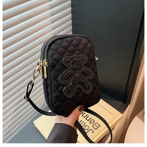 Detail of black quilted crossbody bag featuring a sequin bear patch and double zippers