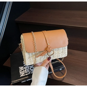 Detail of woven straw shoulder bag with brown leather flap and golden chain strap