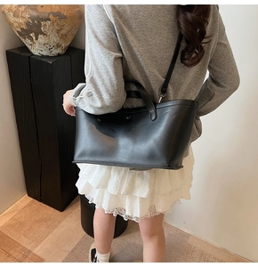 Detailed side view of a black matte leather tote bag with top handle and shoulder strap