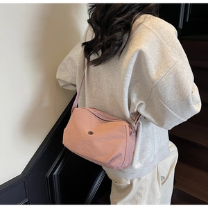 Détail d'un sac bandoulière en nylon rose avec logo métallique porté par un mannequin en scène