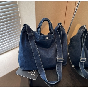 Detailed close-up of dark blue denim tote bag featuring silver snap button and wide strap