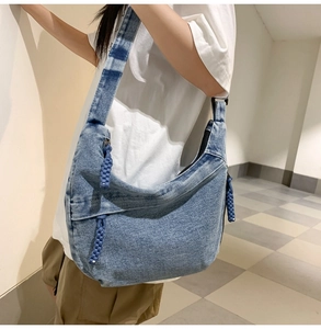 Detail of blue denim crescent bag featuring a woven rope zipper pull and wide strap