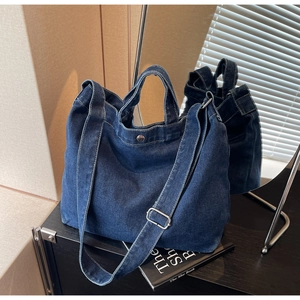 Detail of adjustable metal buckle strap and button on dark blue denim tote bag