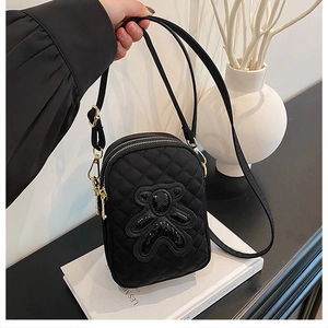 Detail of quilted black phone bag with sequin bear patch and gold double zippers