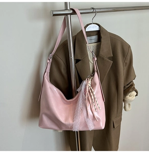 Pink hobo shoulder bag with white lace trim and woven charm hanging on a hanger