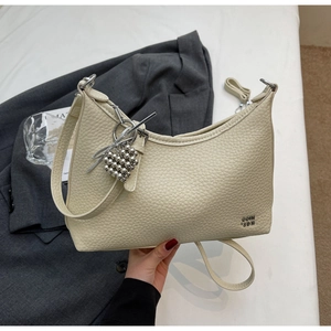 Detail of cream-colored dumpling bag with litchi texture and silver heart charm decoration