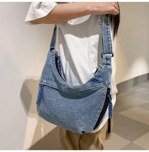 Detail of blue denim crescent crossbody bag with adjustable wide strap and woven zipper puller