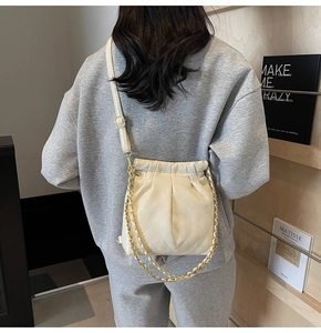 Détail du sac seau matelassé crème avec chaîne dorée et cordon de serrage porté par un mannequin