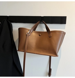 Detail of a brown leather tote bag with round snap button and adjustable strap