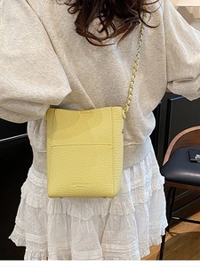 Light yellow lychee leather bucket bag with chain strap shown in cross-body style