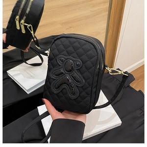 Detail of black quilted crossbody bag featuring a sequined bear and dual zipper pockets