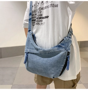 Detail view of washed blue denim texture and moon-shaped sling bag with woven zipper puller