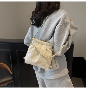 Detail of cream quilted patent leather bucket bag with gold chain strap on shoulder