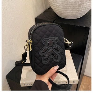 Detail of black quilted phone bag featuring a sequin bear patch and gold double zippers