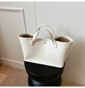 Close-up of a white faux leather tote bag with lychee texture and round buckle detail
