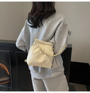 Vue détaillée du sac seau matelassé crème avec chaîne dorée portée à l'épaule