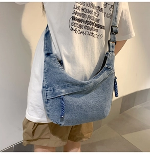 Detail of blue denim crescent bag featuring a wide shoulder strap and woven zipper pull