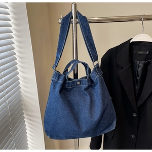 Detail view of denim tote bag with metal buckles hanging against a minimalist background