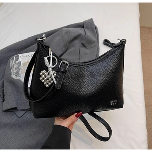 Close-up of black lychee texture crossbody bag with heart bead and bow charm accessory