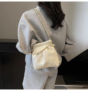 Detail of a beige quilted bucket bag with gold chain strap on a model's shoulder