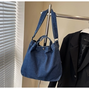 Detail view of dark blue denim tote bag with metal snap button and sturdy wide shoulder strap