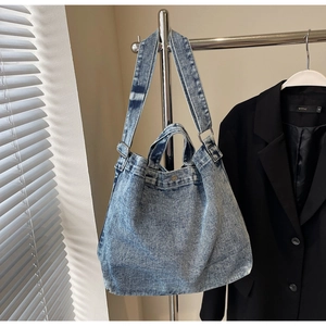 Detail of blue denim tote bag featuring silver snap button and adjustable shoulder strap