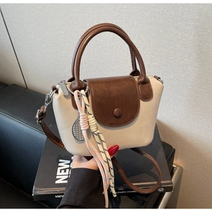 Detail of two-tone contrast crossbody bag featuring a woven rope tennis racket charm
