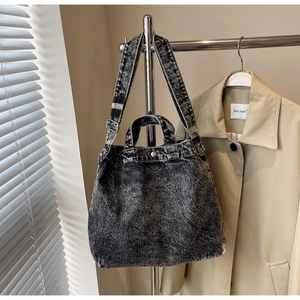 Detail view of washed denim tote bag with metal buckles hanging on a display stand