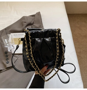Close-up of black quilted drawstring shoulder bag with golden chain and glossy leather texture