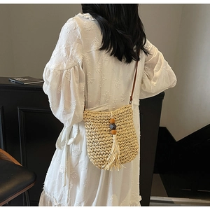 Dettaglio della borsa a tracolla in paglia intrecciata con lunghe nappe e perle di legno