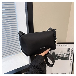 Détail d'un sac bandoulière noir minimaliste avec pendentif cœur et lettrage blanc