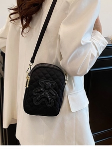 Minimalist black quilted crossbody bag with sequin bear decor worn by model