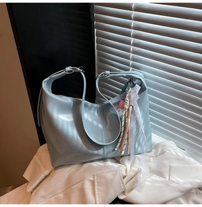 Light blue hobo bag with lace charm accessory placed on a white blazer background