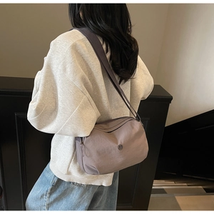 Sac bandoulière en nylon mauve porté par un mannequin dans un escalier moderne