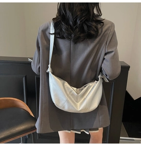 Detail view of silver crescent crossbody bag with distinctive knot strap on a model shoulder