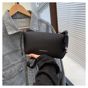 Détail du sac à bandoulière noir montrant la texture mate et le pendentif en métal argenté