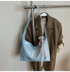 Detail of light blue patent leather hobo bag with lace bow and striped pendant charm