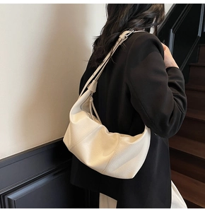 Detail view of cream leather crescent shoulder bag with pleated design on a model