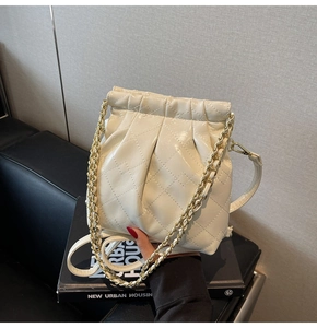 Détail d'un sac seau matelassé beige avec cordon de serrage et chaînes dorées
