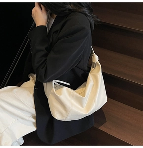 Detail of the soft off-white shoulder bag with knot strap design on a black blazer