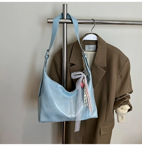 Detail of light blue glossy hobo bag with lace ribbon and heart pendant on shoulder strap