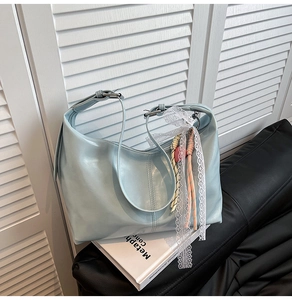 Close-up of light blue hobo bag with white lace ribbon and colorful woven charm