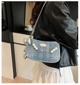 Détail du sac d'épaule en denim bleu avec chaîne de perles et charms argentés