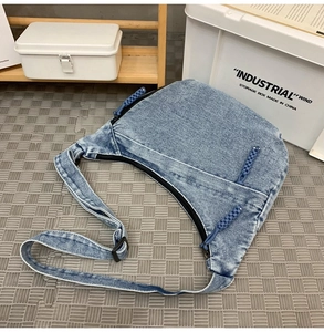 Detail of blue denim crescent bag featuring multiple zip pockets and woven pullers