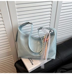 Detail of light blue hobo bag with white lace bow and adjustable strap on a leather sofa